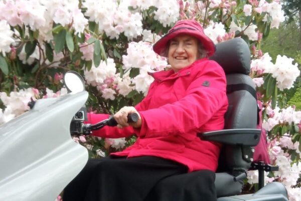 Liz, Countryside Mobility members in a Tramper surrounded by blooming flowers
